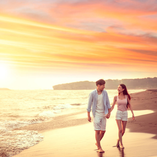 Mutlu Asyalı genç çift gün batımında sahilde yürüyor. - Fotoğraf, Görsel