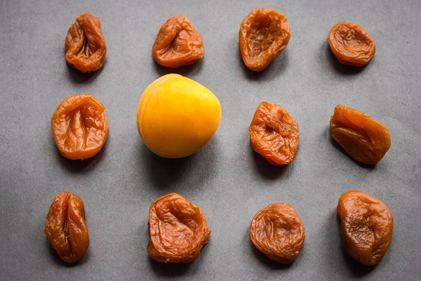 Yellow apricot with smooth skin among wrinkled, dried fruits. Youth, beauty, freshness. Dark background, daylight. - Photo, Image
