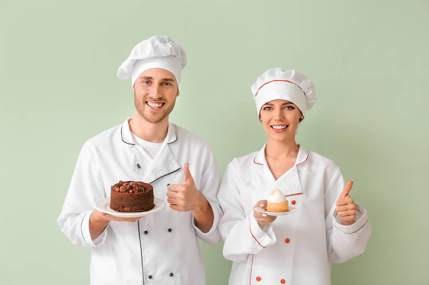 Young confectioners with tasty desserts showing thumb-up gesture on color background - Photo, image