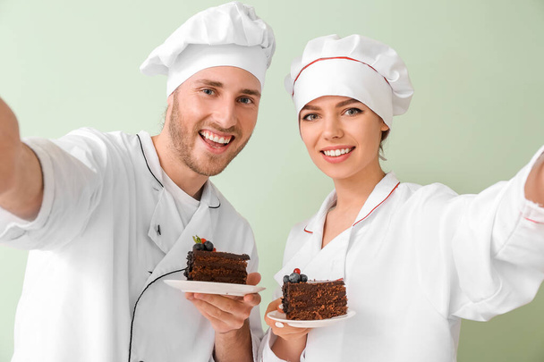 Young confectioners with tasty dessert taking selfie on color background - Photo, Image