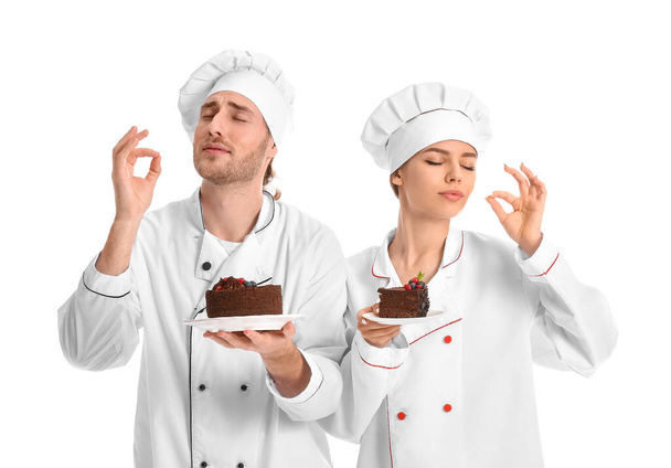 Young confectioners with tasty desserts on white background - Photo, Image