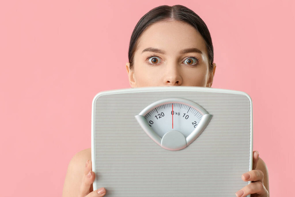 Shocked young woman with measuring scales on color background - Photo, Image