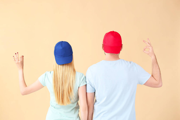 Νεαρό ζευγάρι με κομψά καλύμματα που δείχνουν OK χειρονομία στο φόντο χρώμα, προβολή πίσω - Φωτογραφία, εικόνα