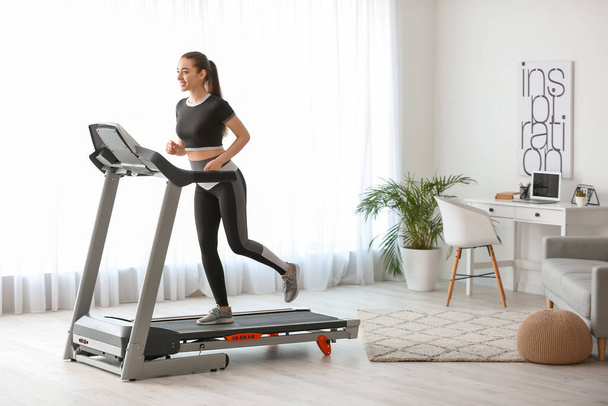 Sporty young woman training on treadmill at home - 写真・画像
