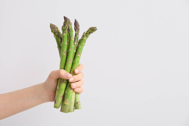 Hand with fresh asparagus on light background - Фото, изображение
