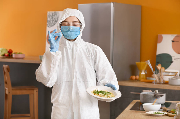 Woman in biohazard suit cooking in kitchen - Фото, зображення
