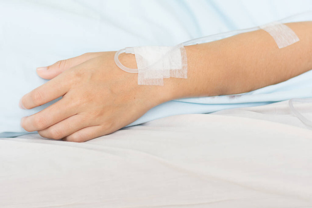 Zbliżyć roztwór soli fizjologicznej na ręce pacjentki w niebieskich ubraniach leżącej na szpitalnym łóżku. Dostarczanie składników odżywczych do naczyń. - Zdjęcie, obraz