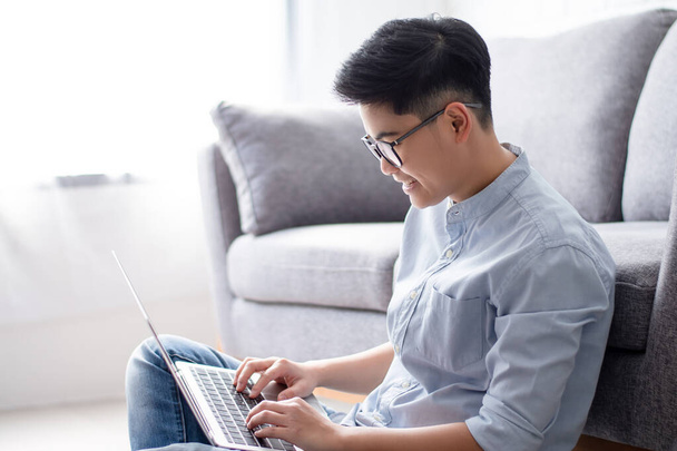 Asian man sitting on the floor and working on a computer laptop at home with copy space. - Foto, Imagem