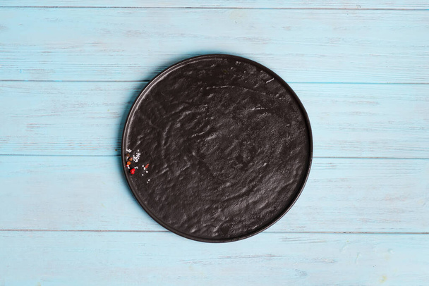 Bovenaanzicht van donkere keramische plaat met specerijen en zout op een lichtblauwe houten ondergrond. - Foto, afbeelding
