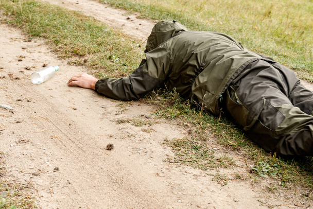 um homem rastejante em uma estrada de campo alcança para uma garrafa. desejo de álcool
 - Foto, Imagem