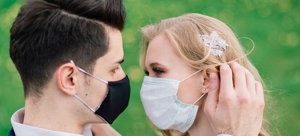 Nuori rakastava pari kävelee lääketieteellisissä naamioissa puistossa hääpäivänään karanteenin aikana. Koronavirus, sairaus, suojelu, sairas. Euroopan juhlallisuudet peruttu. - Valokuva, kuva