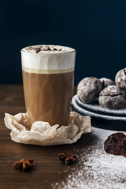 A few marble brown cookies with glass of coffee latte, star anise and powdered sugar on wooden background - Photo, Image