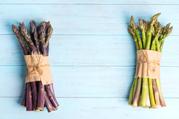 Świeże naturalne organiczne dwa pakiety zielonych i fioletowych warzyw szparagowych na niebieskim drewnianym tle. - Zdjęcie, obraz