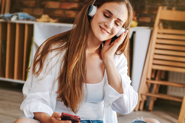 Художественная счастливая женщина в наушниках слушает музыку, наслаждается звуком смартфона
 - Фото, изображение