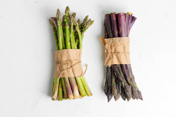 Świeże naturalne organiczne dwa pakiety zielonych i fioletowych warzyw szparagowych na kamiennym tle. - Zdjęcie, obraz