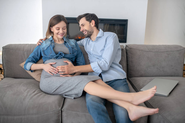 Young pregnant woman in a jeans jacket feeling great with her husband at home - Foto, Imagem