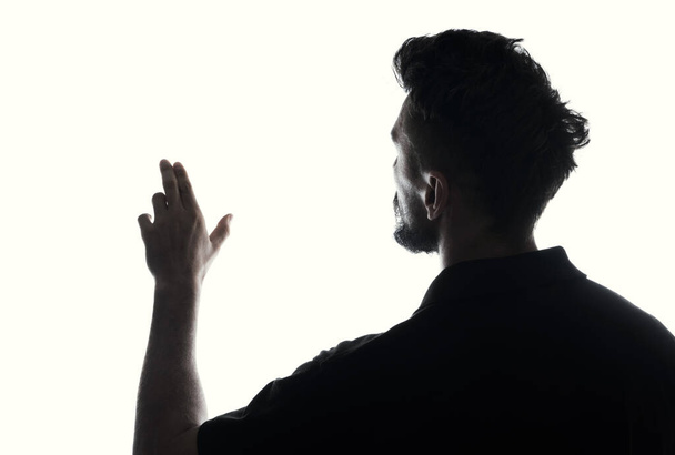 Silhouet van een man raakt lege ruimte met de hand, achteraanzicht verlicht over wit  - Foto, afbeelding