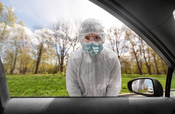 healthcare worker in hazmat suit looking into car - Fotó, kép
