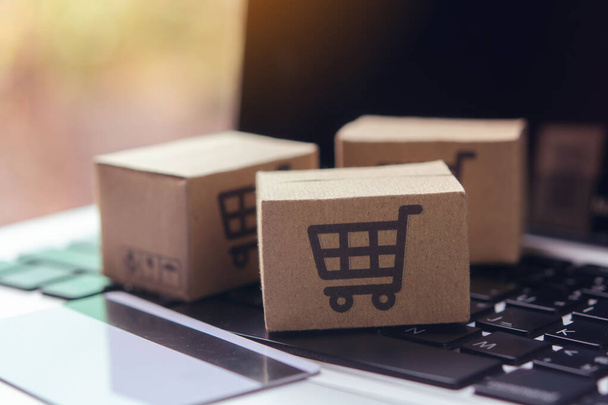 Online shopping - Paper cartons or parcel with a shopping cart logo and credit card on a laptop keyboard. Shopping service on The online web and offers home delivery. - Photo, image