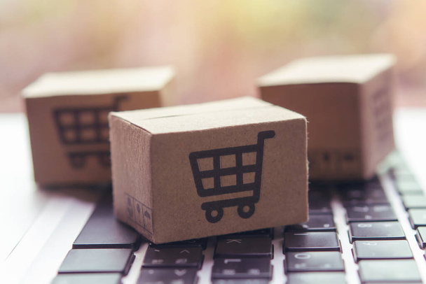 Online shoppen - Papieren doosjes of pakketjes met een winkelwagen logo op een laptop toetsenbord. Winkelen op het online web en biedt levering aan huis. - Foto, afbeelding
