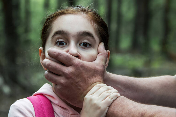 Child abduction. A man puts his hand over the mouth of a terrified teenage girl in a pink sweatshirt. The concept of kidnapping. Close up. - 写真・画像