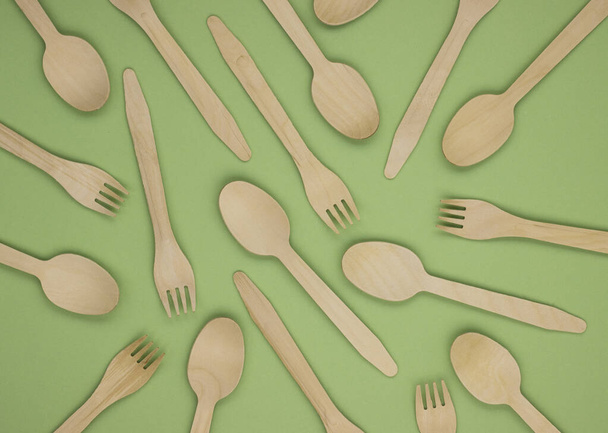 Eco-friendly disposable tableware made of bamboo wood and paper on a green background. Draped spoons and forks. The concept of zero waste. Preserving the purity of nature - Foto, immagini