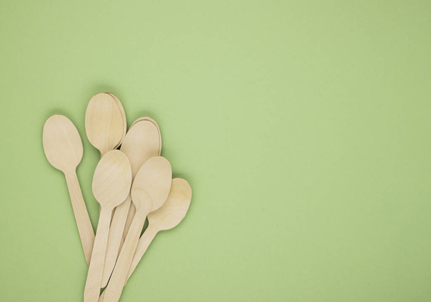 Eco-friendly disposable tableware made of bamboo wood and paper on a green background. Draped spoons scattered on the table. The concept of zero waste. Preserving the purity of nature - Foto, Imagem