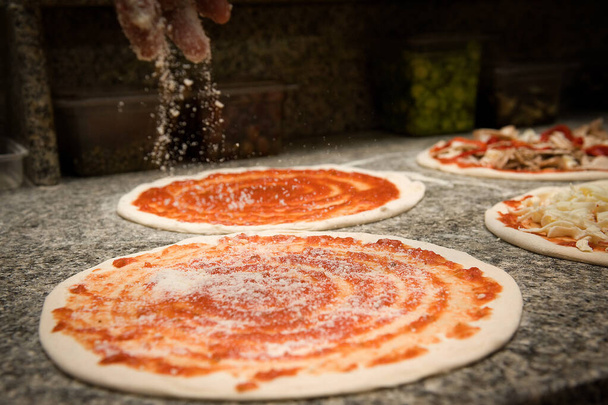 Pizzacı domates sosuna parmesan koyarak İtalyan pizzası hazırlar. - Fotoğraf, Görsel
