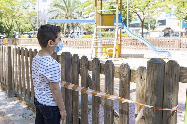 Θλιμμένο αγόρι μπροστά σε μια κλειστή παιδική χαρά - Φωτογραφία, εικόνα