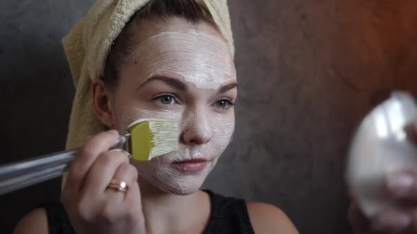 eine junge Frau bekommt cremefarbene Schönheit weiße Maske aus saurer Sahne mit einem Pinsel - Filmmaterial, Video