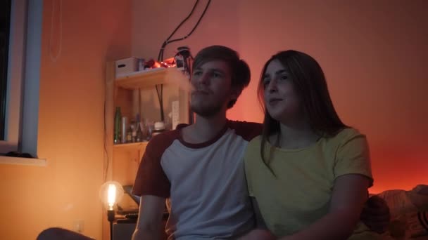 Young man and woman watching film at home talking with chips - Materiał filmowy, wideo