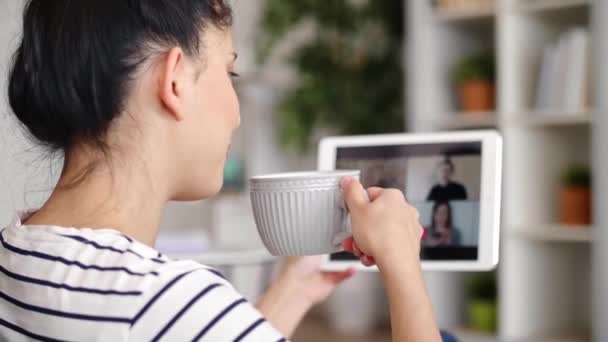 Tilt up video van vrouw die koffie drinkt tijdens video conferentie - Video
