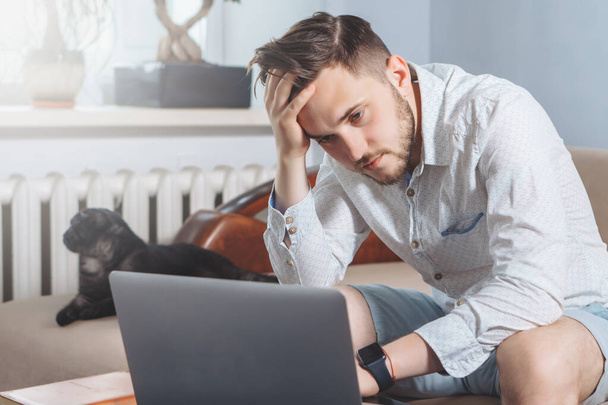 Fáradt fiatal szabadúszó laptopot használ, miközben otthonról dolgozik - Fotó, kép
