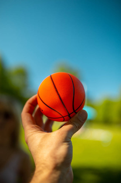 Bright orange mini basketball in a hand against blue sky - Fotoğraf, Görsel