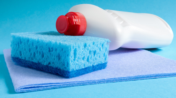 Ein blauer Schwamm mit einer weißen Flasche Waschmittel auf blauem Hintergrund. Die Bequemlichkeit der Schwämme besteht in einer guten Reinigungsmittelbindung, die es ermöglicht, sie wirtschaftlich zu verwenden. - Foto, Bild