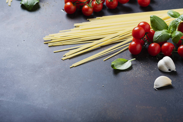 Ingredients for cooking italian pasta: spaghetti, tomato, basil and garlic on the black table. Selective focus image with a copy space - Valokuva, kuva