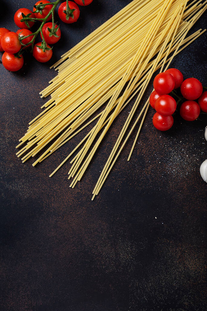 Ingredients for cooking italian pasta: spaghetti, tomato and garlic on the black table. Top view image with a copy space - 写真・画像