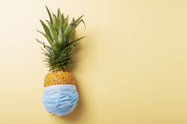 Concept of summer vacation 2020. Pine apple with a medical mask on the yellow background. Top view image - Valokuva, kuva