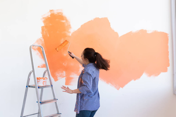 Dancing funny young woman painting interior wall with paint roller in new house. A woman with roller applying paint on a wall. - Photo, Image