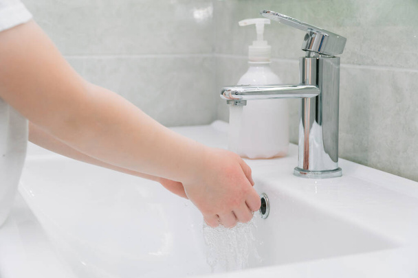 Child washes hands a small with soap over the sink with running water. Personal hygiene. Protection against COVID-19 - Фото, изображение
