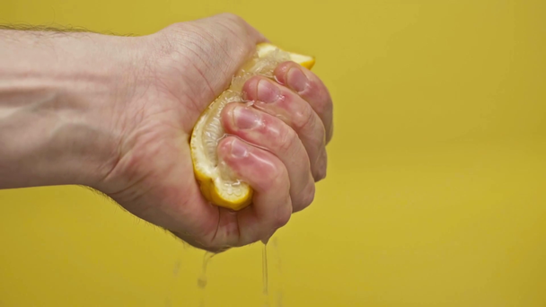 mužská ruka mačkající citron izolovaný na žlutém, zpomaleném filmu - Záběry, video
