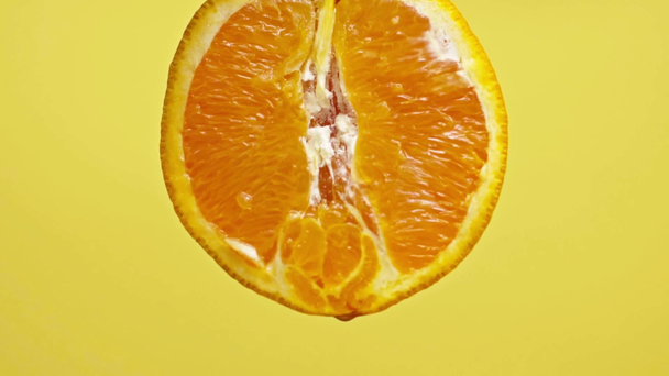 黄色のスローモーションで隔離されたオレンジの半分から滴り落ちるジューシーな滴 - 映像、動画