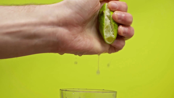 male hand squeezing lime juice in glass isolated on green, slow motion - Footage, Video