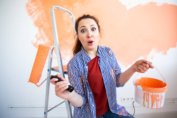 Engraçado jovem pintando parede interior com rolo de pintura em casa nova. Uma mulher com rolo aplicando tinta em uma parede
. - Foto, Imagem