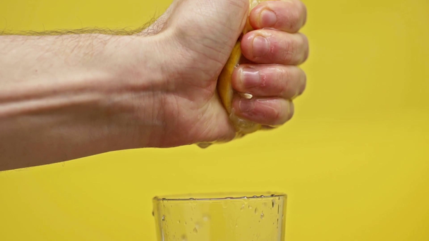 male hand squeezing lemon juice in glass isolated on yellow, slow motion - Кадры, видео