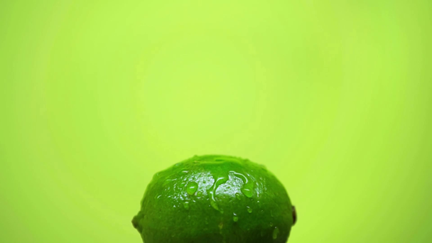 drops falling on whole ripe lime isolated on green, slow motion - Footage, Video