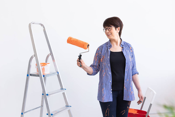 Preciosa mujer de mediana edad pintando la pared. Concepto de renovación, redecoración y reparación. - Foto, imagen