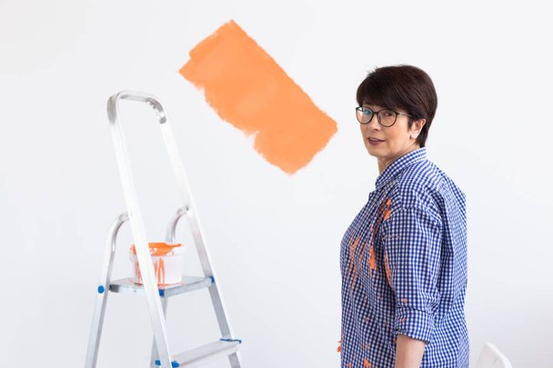 Naprawa w mieszkaniu. Szczęśliwa kobieta w średnim wieku maluje ścianę farbą. - Zdjęcie, obraz