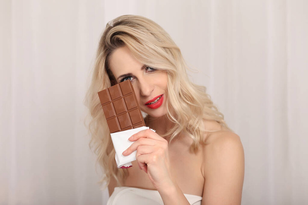 Atrakcyjny blond studio portret jedzenie czekolady na jasnym tle - Zdjęcie, obraz