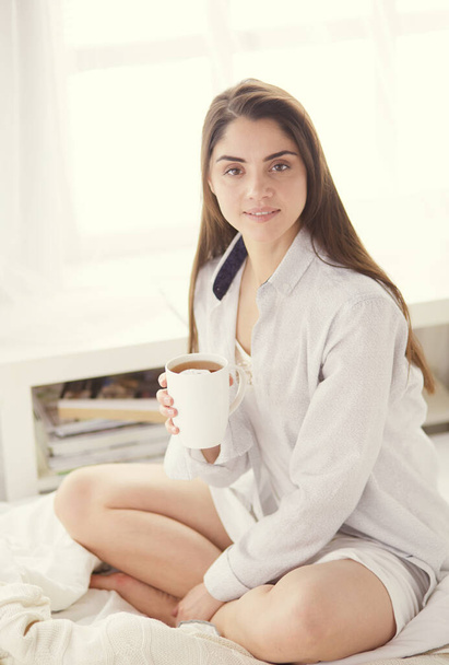 Woman sitting in bed reading a book and having breakfast - Foto, imagen